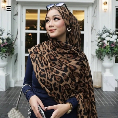 Woman wearing a leopard print hijab in front of a building with flowers.